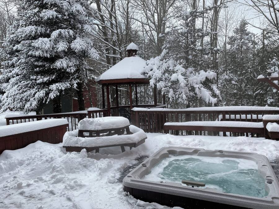 A snow-covered outdoor area with a hot tub, wooden deck, and a gazebo.