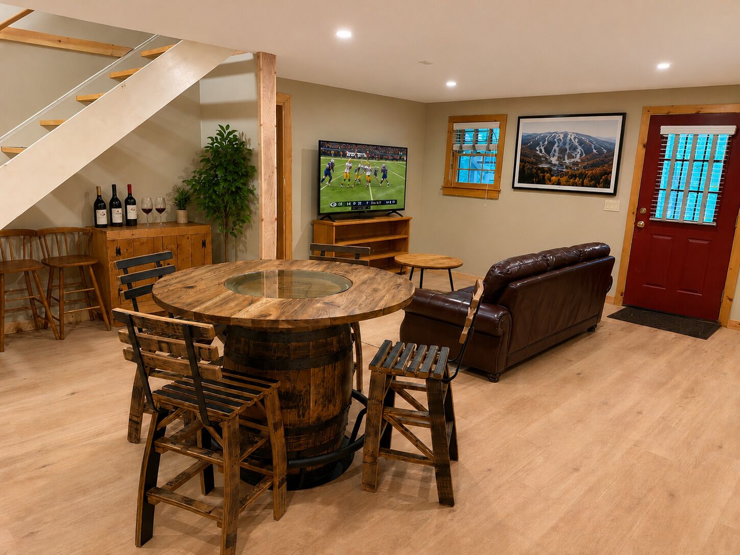 A dining area with a wooden table, chairs, a sofa, a TV, and a staircase.