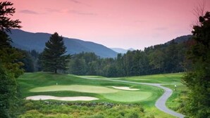 Un campo de golf con un camino sinuoso, rodeado de árboles y montañas.