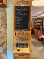 Una exhibición de madera con un menú en pizarra que enumera productos horneados e infusiones de hierbas, y botellas de especias de calabaza y otros sabores.