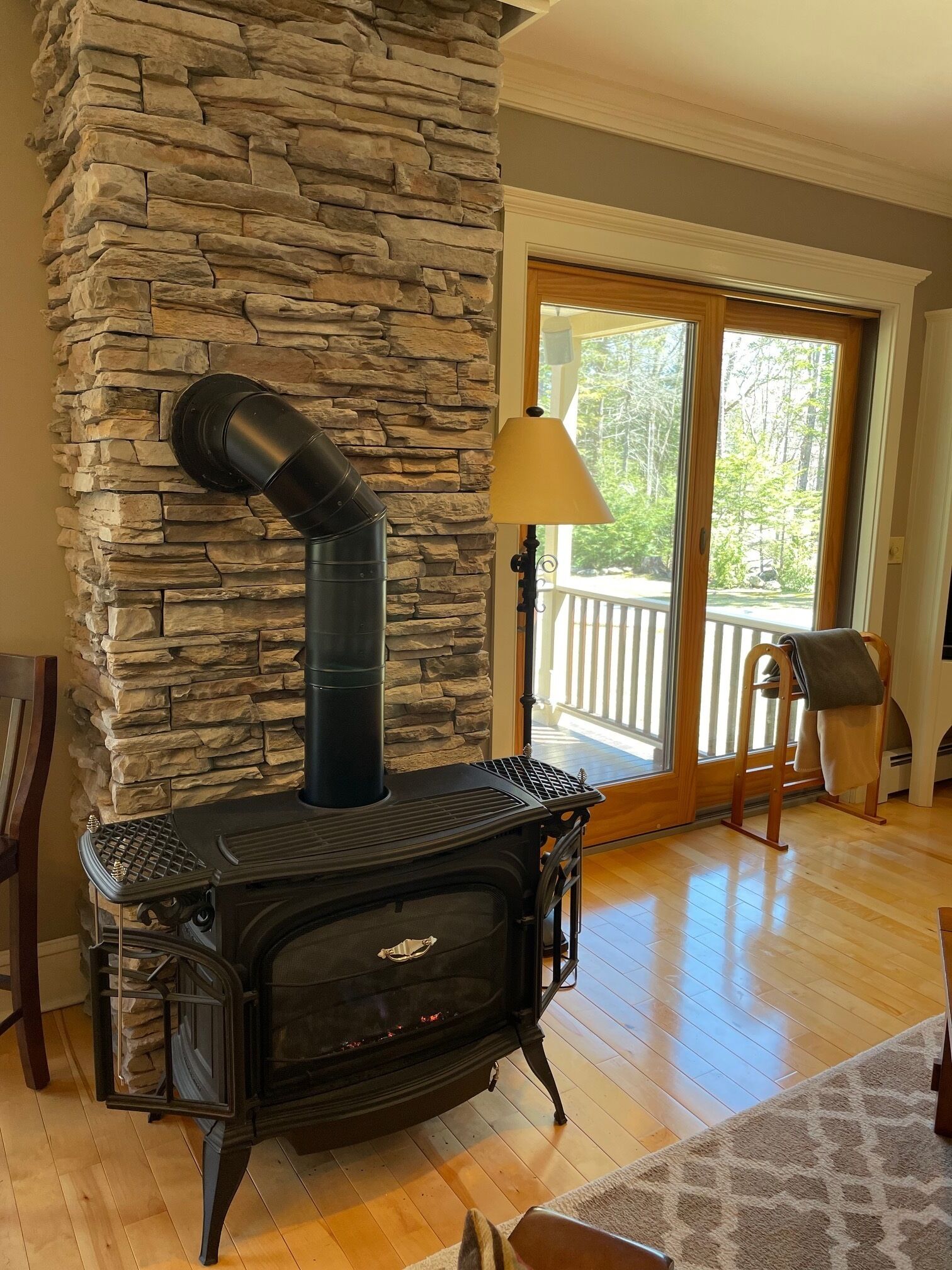 A stone fireplace with a black chimney, a wooden bench, and a view of a balcony with a railing.
