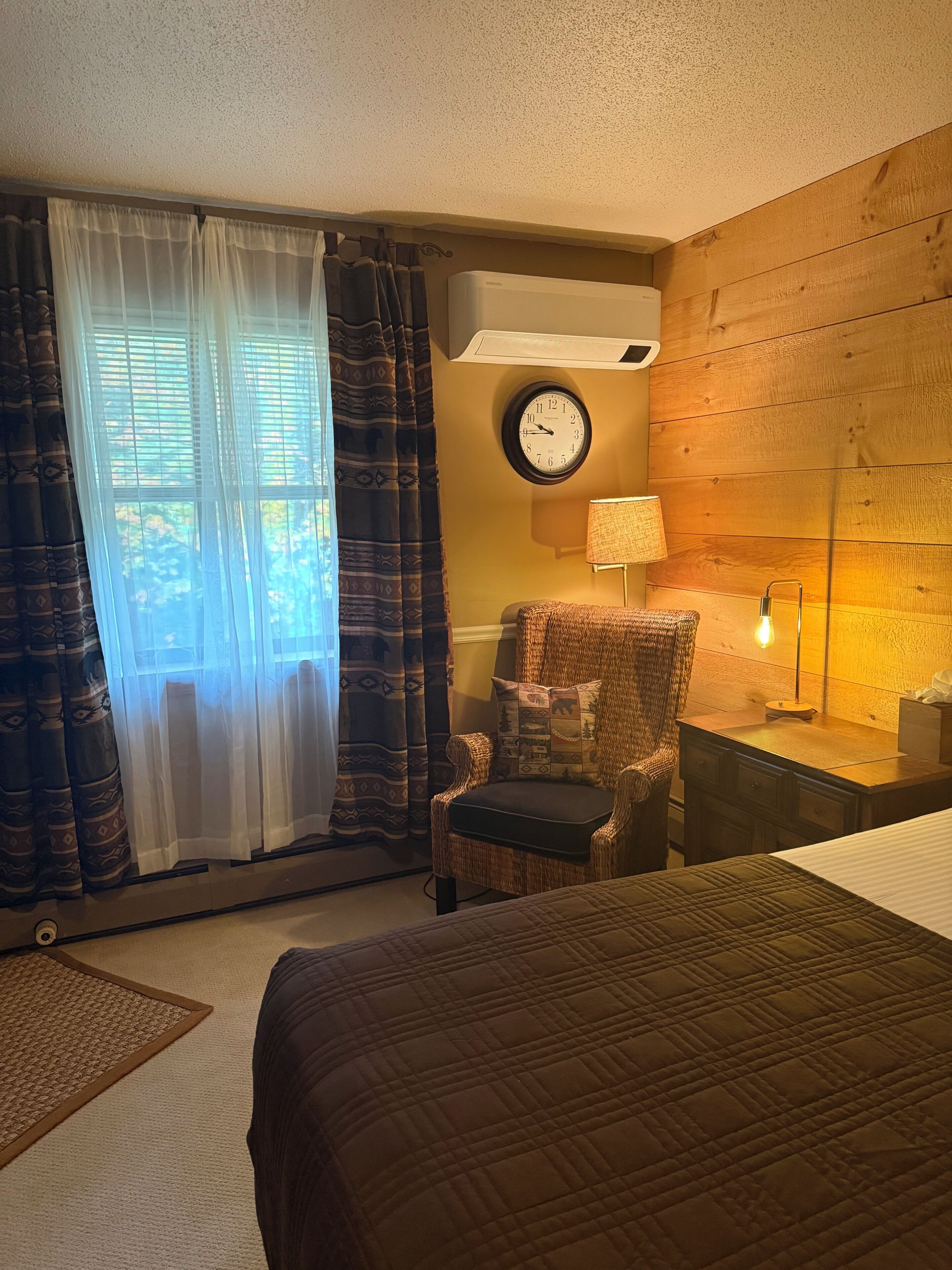 Una habitación de hotel con una cama, una silla, un reloj y una lámpara.