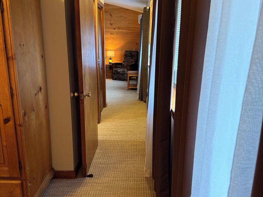 A hallway with wooden doors and a carpeted floor leading to a room with a lamp and a chair.