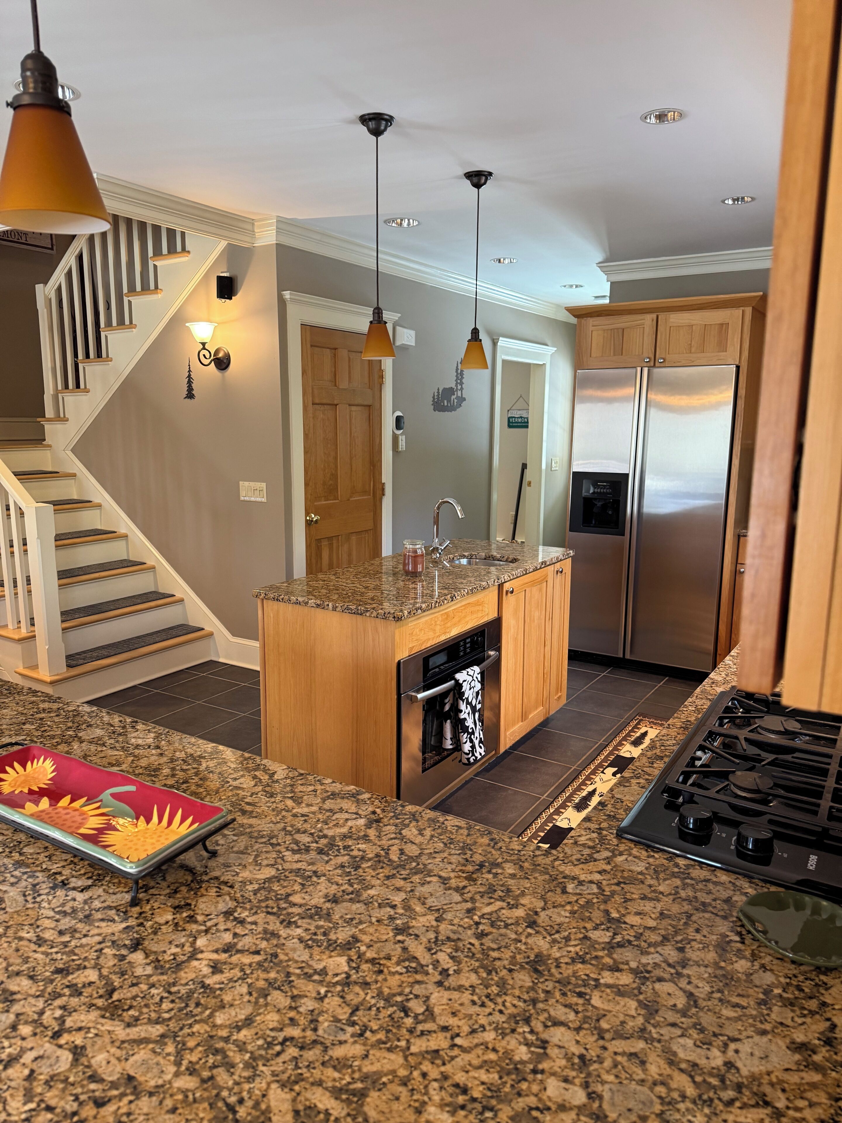 A kitchen with granite countertops, a built-in oven, a stainless steel refrigerator, and a wooden island.