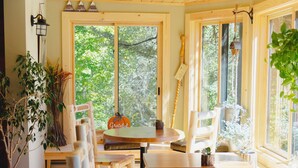 Un interior de madera con zona de comedor que incluye una mesa redonda y bancos, ventanas amplias con vistas a follaje, y un letrero que dice 'Grateful'.