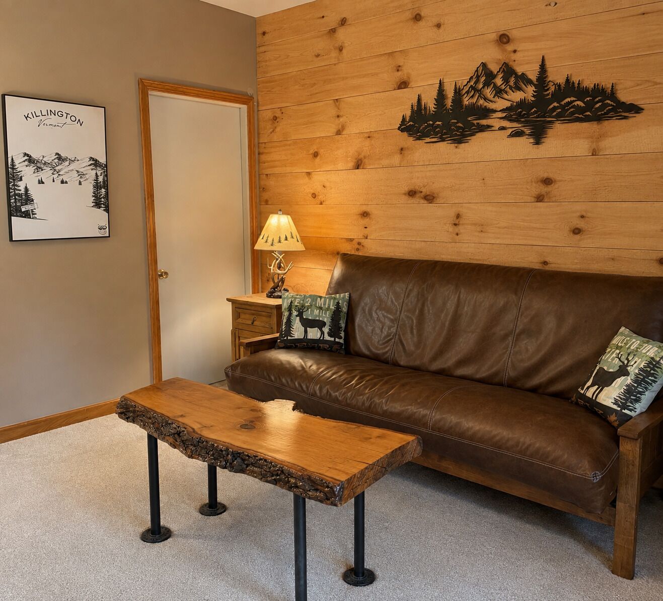 Una habitación acogedora con un sofá de cuero marrón, una mesa de centro de madera, una lámpara y una pared con un mural de paisaje montañoso.