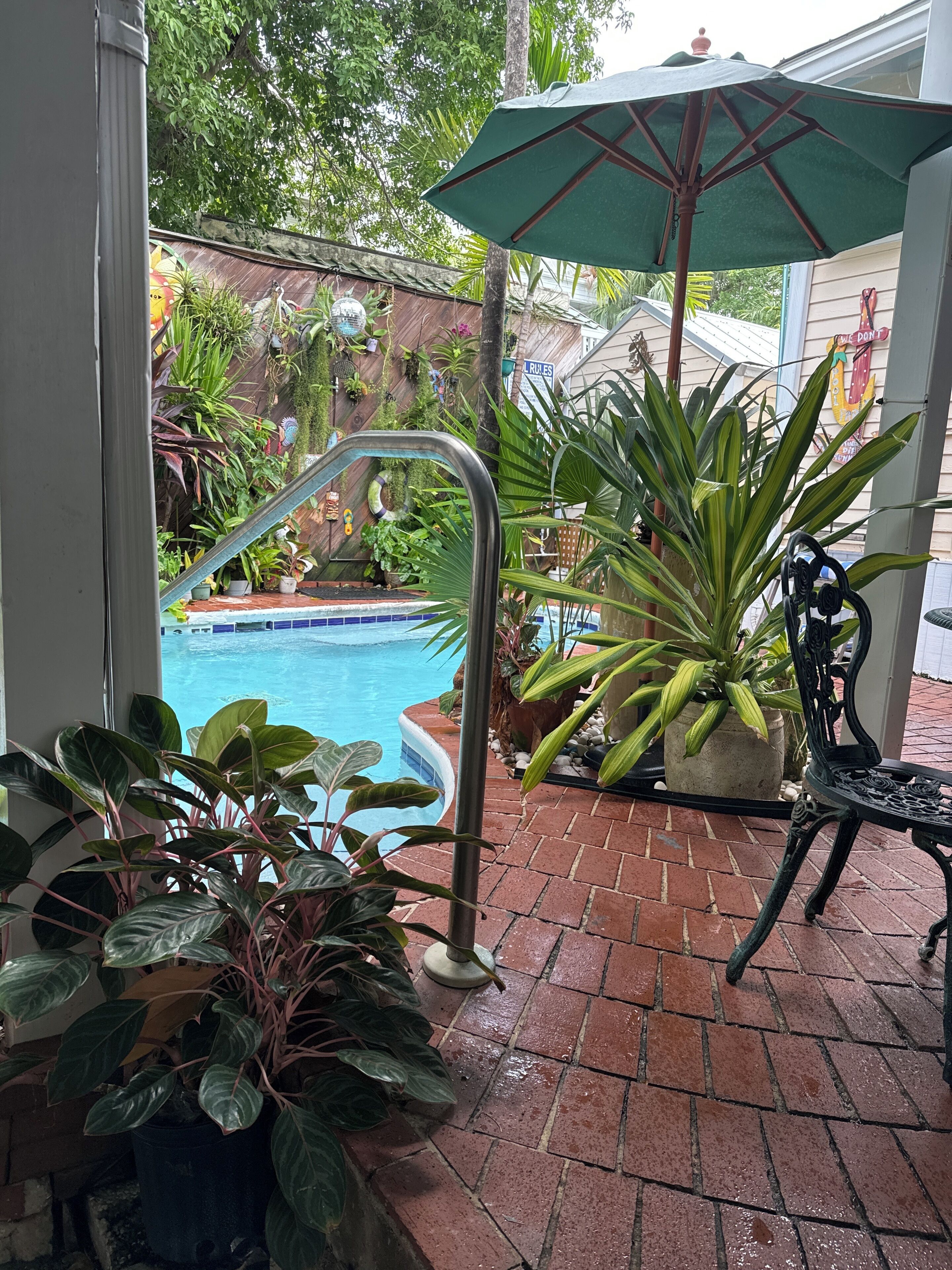 A pool area with a metal staircase leading to the water, surrounded by potted plants and a green umbrella.