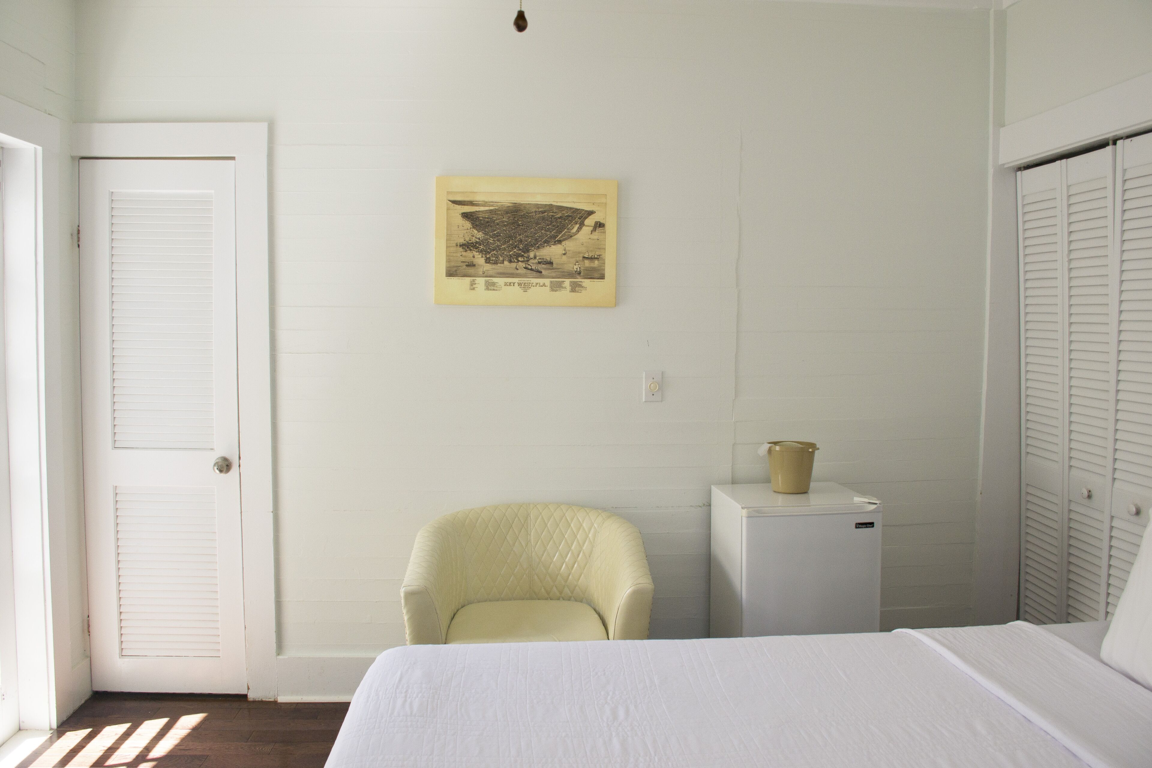A bedroom with a bed, a chair, a small white cabinet, and a wall-mounted picture.