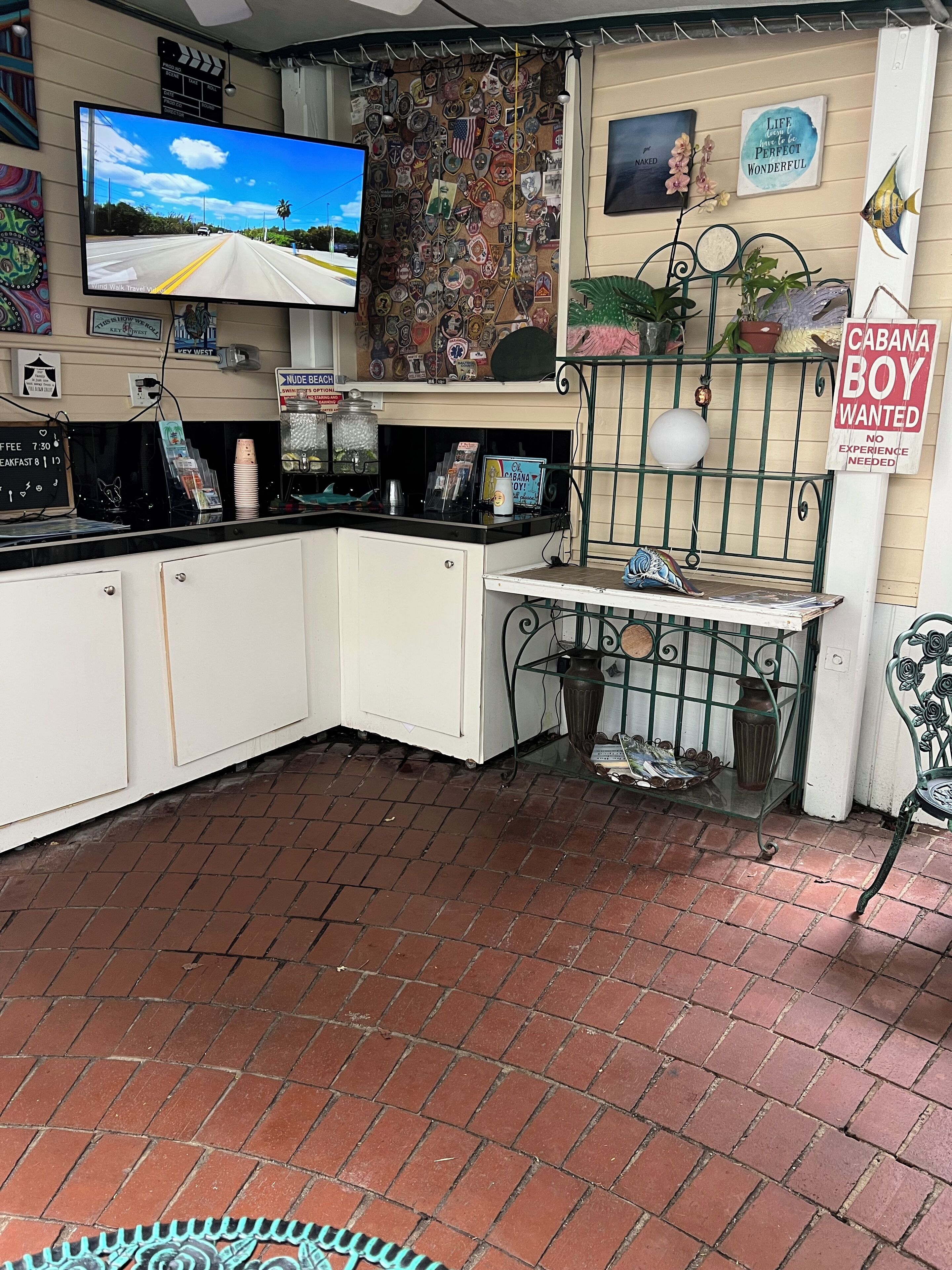 A small, cozy coffee shop with a TV mounted on the wall, a variety of decorations, and a sign advertising a 'Cabana Boy Wanted'.