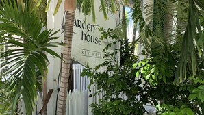 Una cerca blanca de piquetes, una palmera y un letrero que dice 'Garden House Key West'.