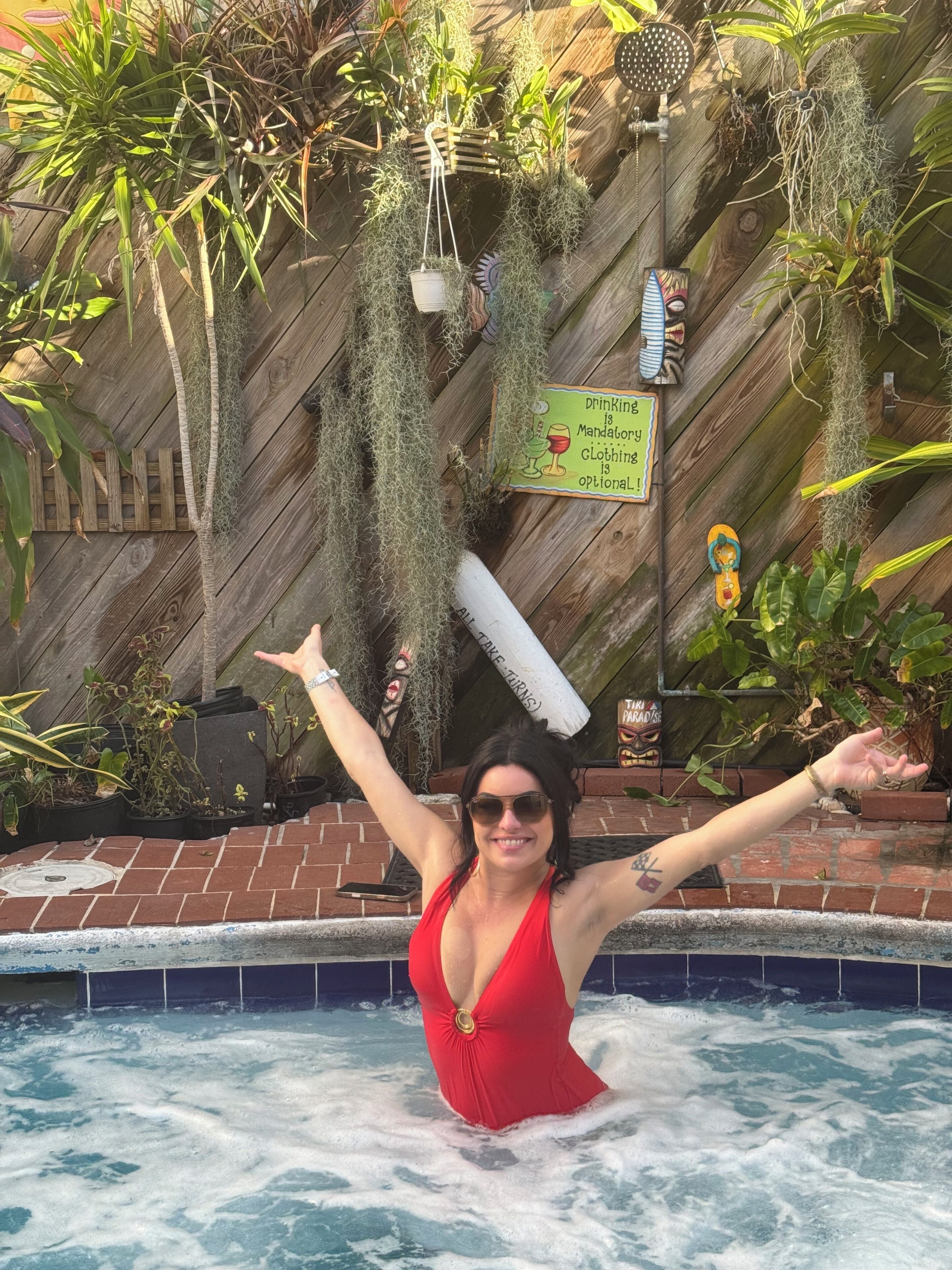A woman in a red swimsuit standing in a pool with her arms raised.