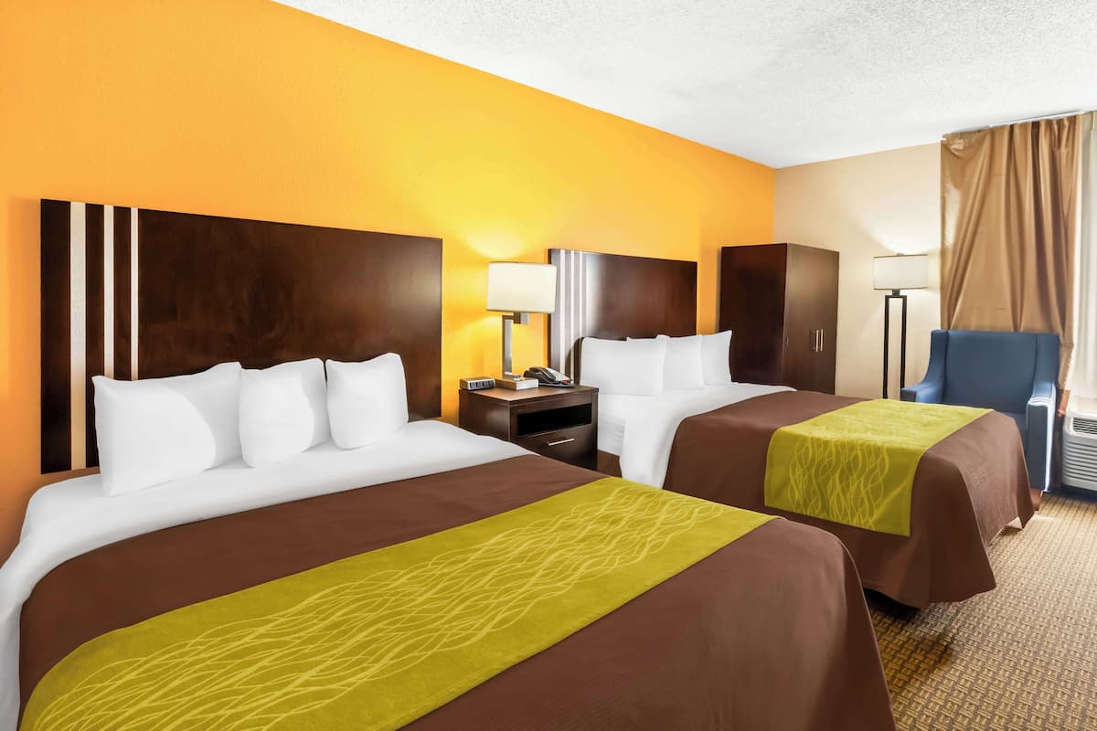 Une chambre d’hôtel avec deux lits, un bureau, une chaise et une lampe.