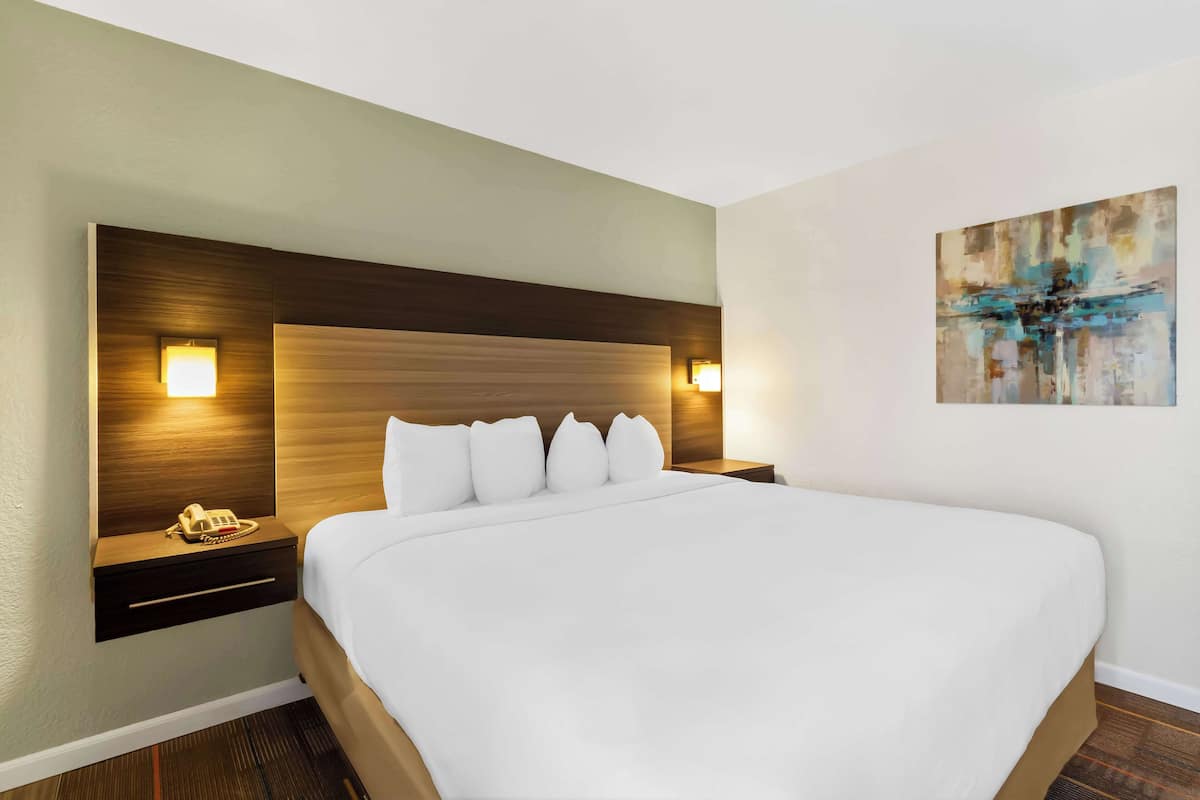 Une chambre d’hôtel avec un grand lit, une tête de lit en bois, des lampes de chevet et un tableau au mur.