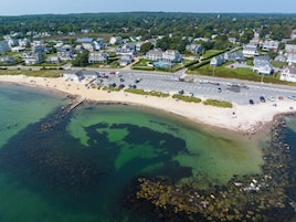 An aerial view of a coastal town with a sandy beach, clear waters, and residential buildings.