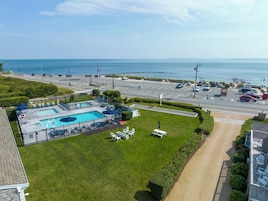 Zona de piscina con varias piscinas y sillas de descanso, rodeada por un césped cuidado y un aparcamiento con coches.