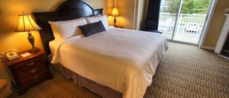 A hotel room with a large bed, two bedside lamps, a wooden nightstand, and a view of a balcony with outdoor furniture.