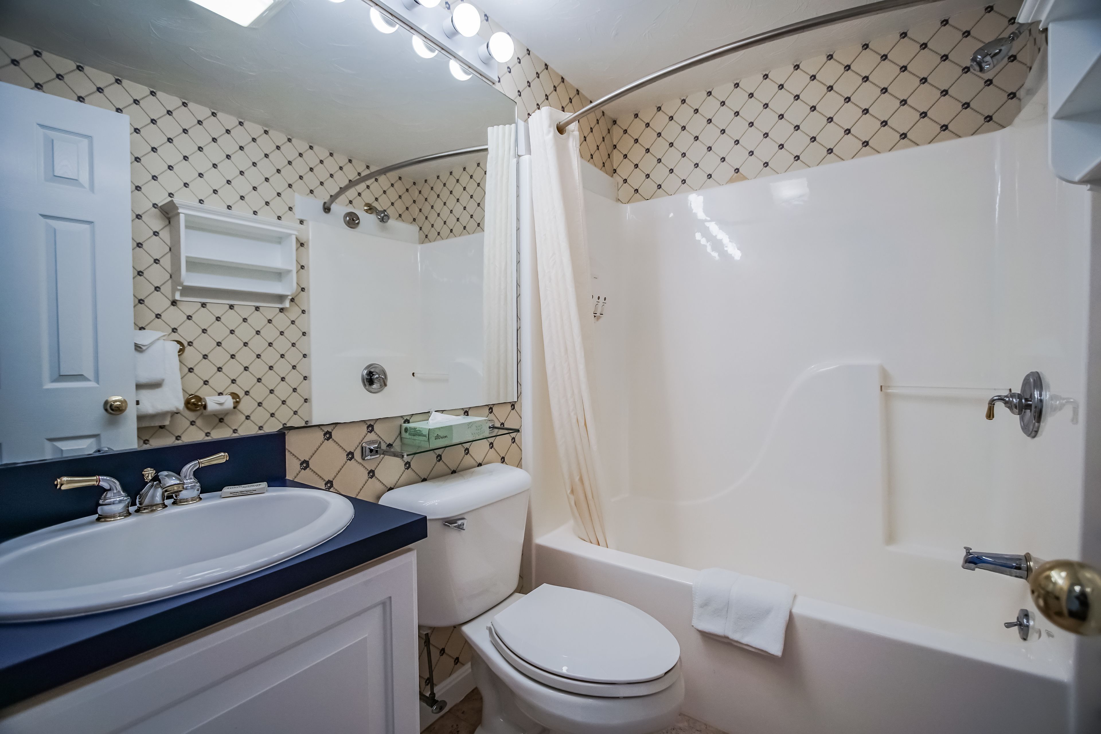 A bathroom with a white sink, toilet, and bathtub, a mirror above the sink, and a shower curtain.