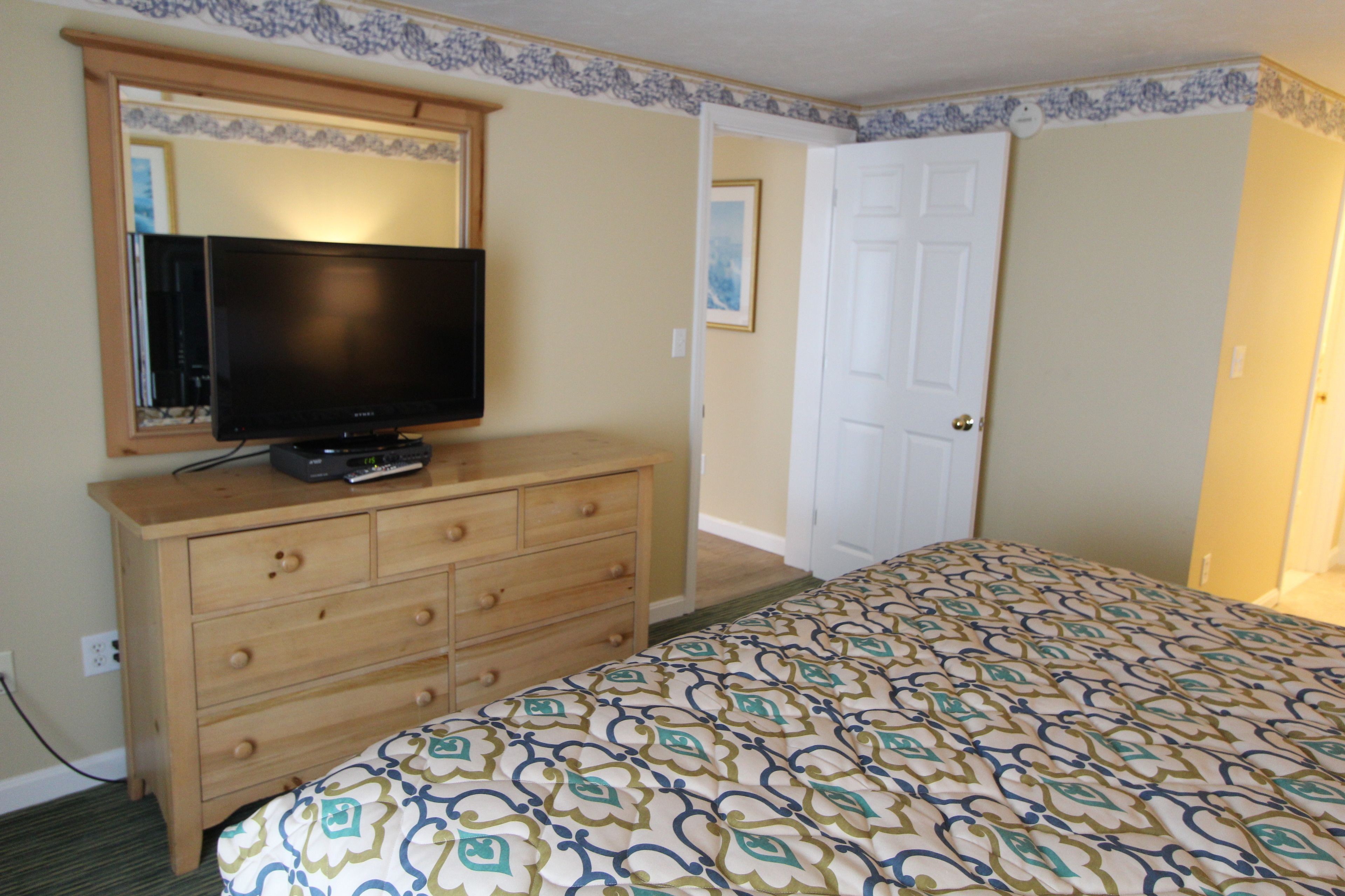 A bedroom with a bed, a dresser, a television, and a door.