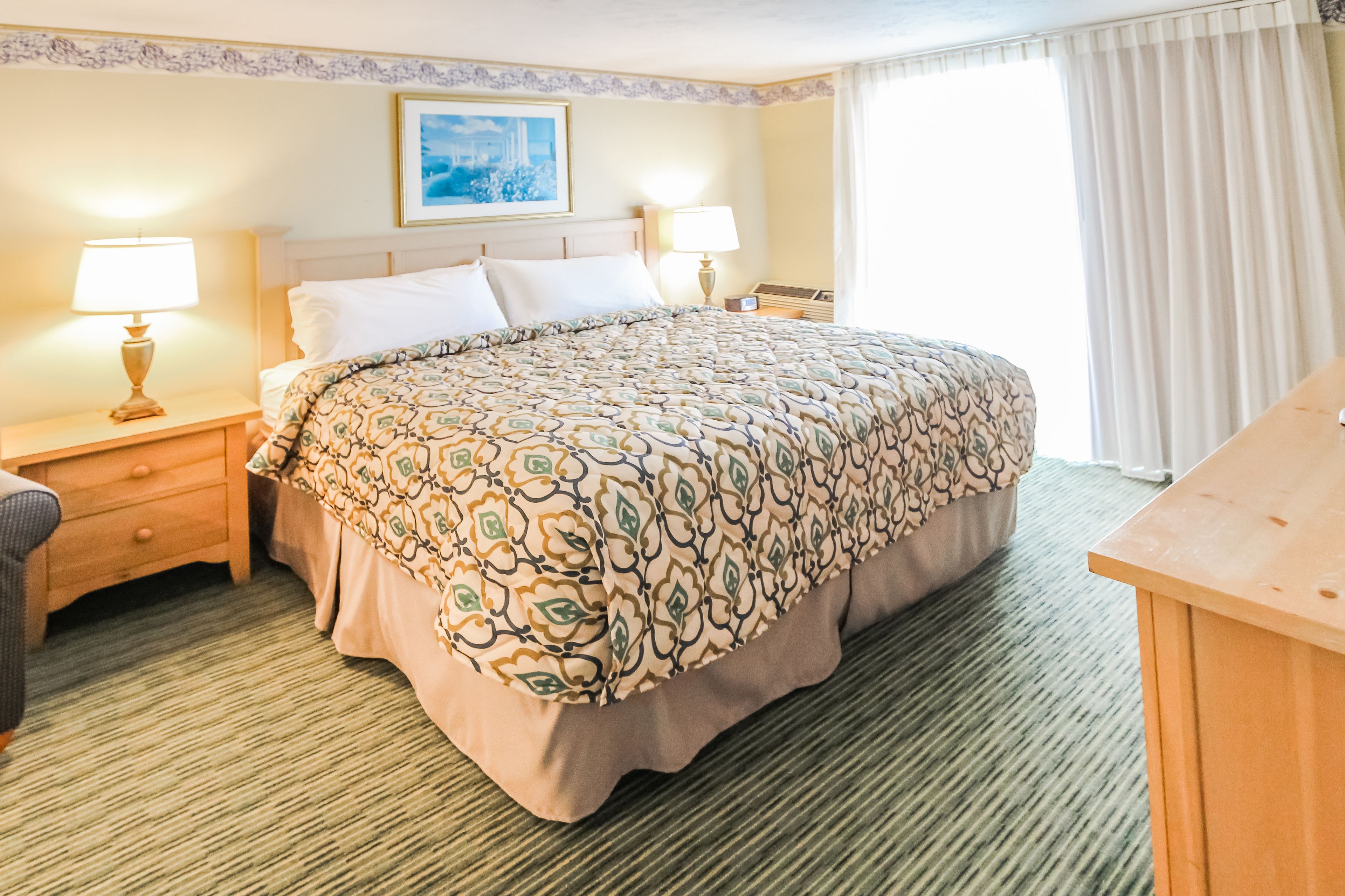 A hotel room with a large bed, two bedside tables with lamps, a wooden desk, and a painting on the wall.