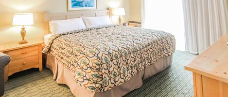 A hotel room with a large bed, two bedside tables with lamps, a wooden desk, and a painting on the wall.