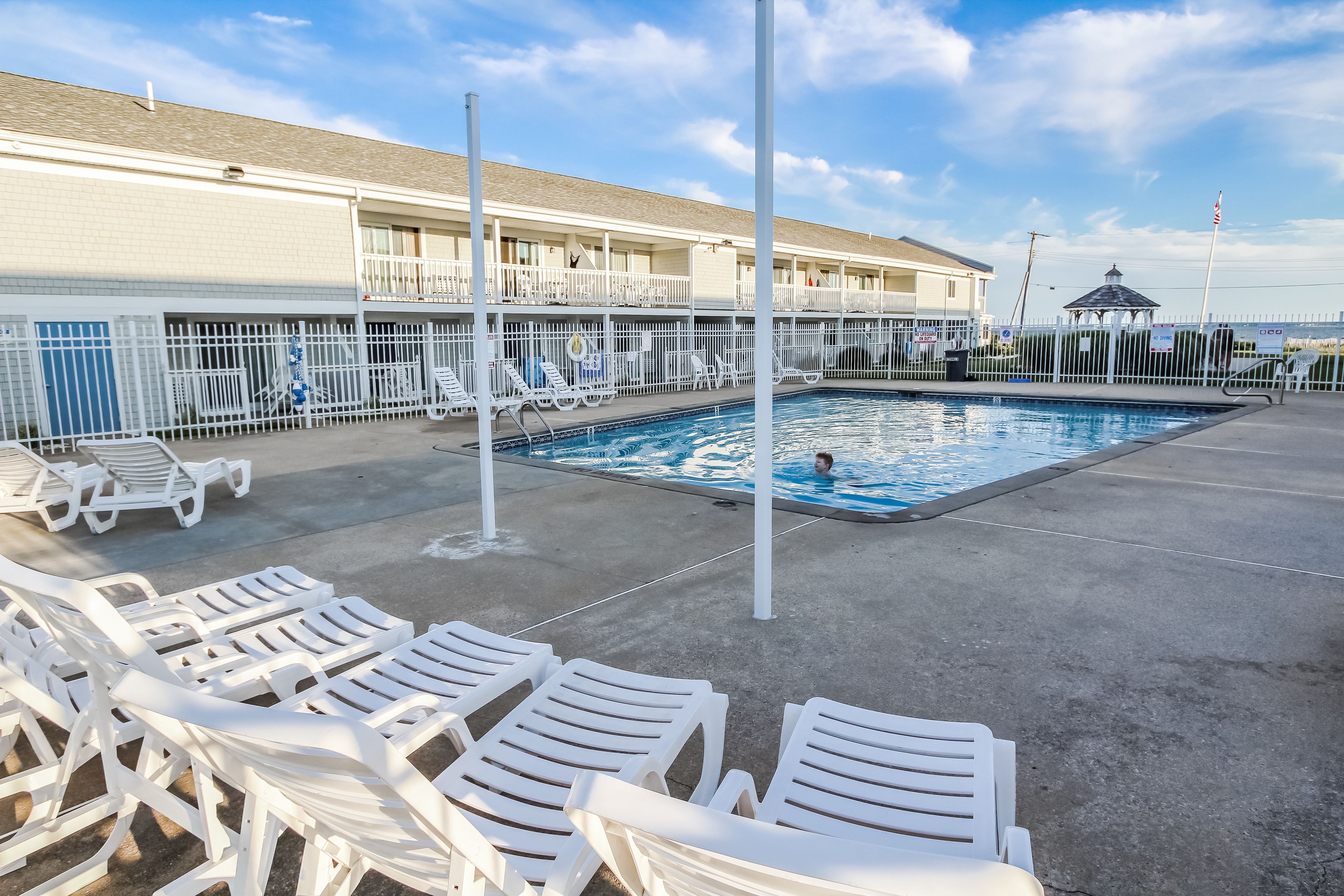 A pool area with white lounge chairs and a building with balconies in the background.