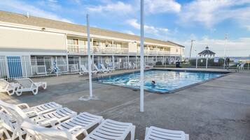 A pool area with white lounge chairs and a building with balconies in the background.