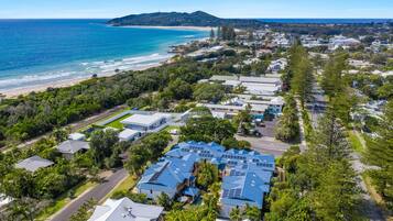 An aerial view of a coastal residential area with houses, a beach, and a hilly landscape in the background.