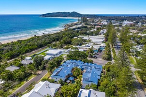 Vista aérea de una zona residencial costera con casas, una playa y un paisaje montañoso al fondo.