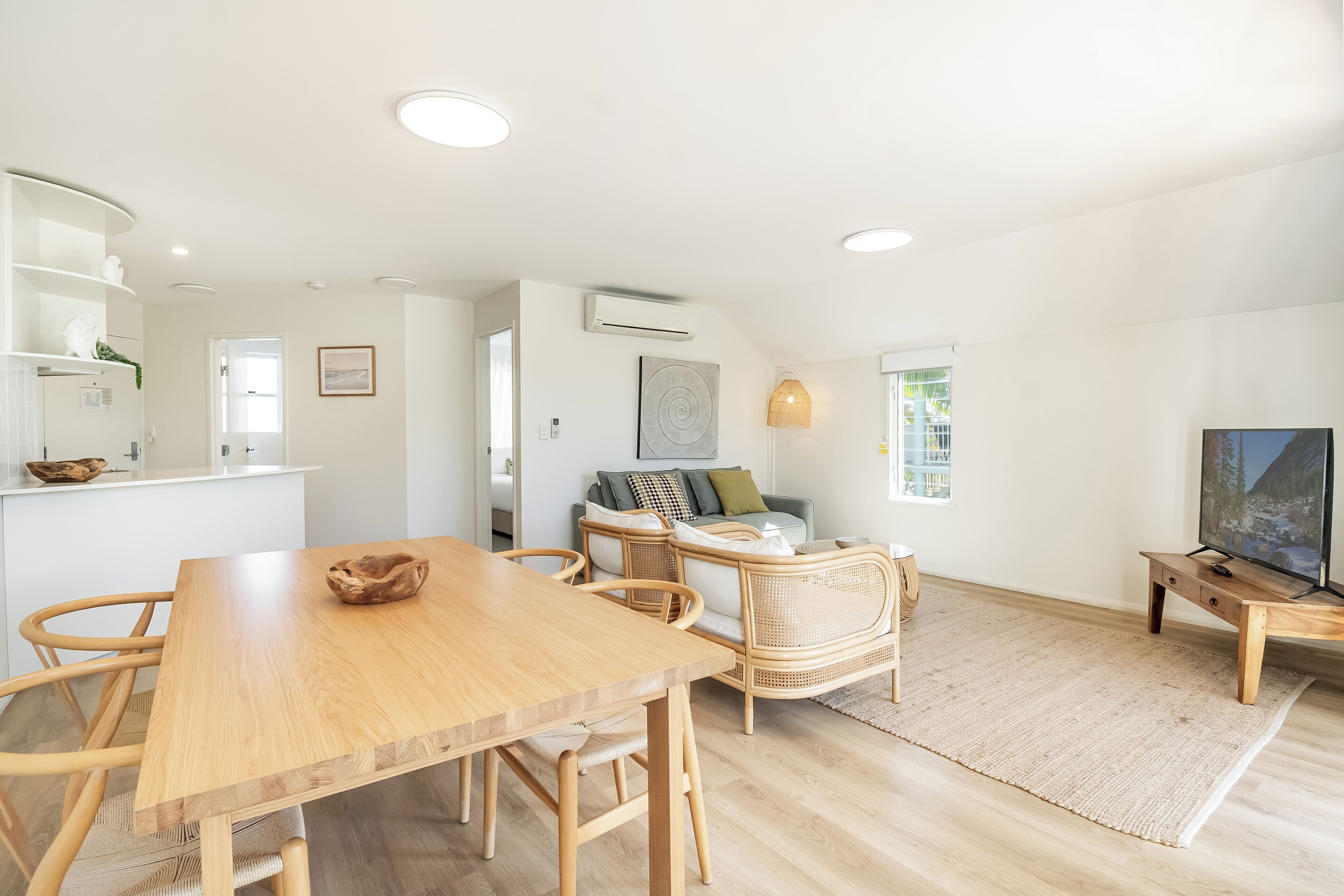 Un espace de vie moderne avec une table à manger en bois, des meubles en osier et un téléviseur à écran plat.
