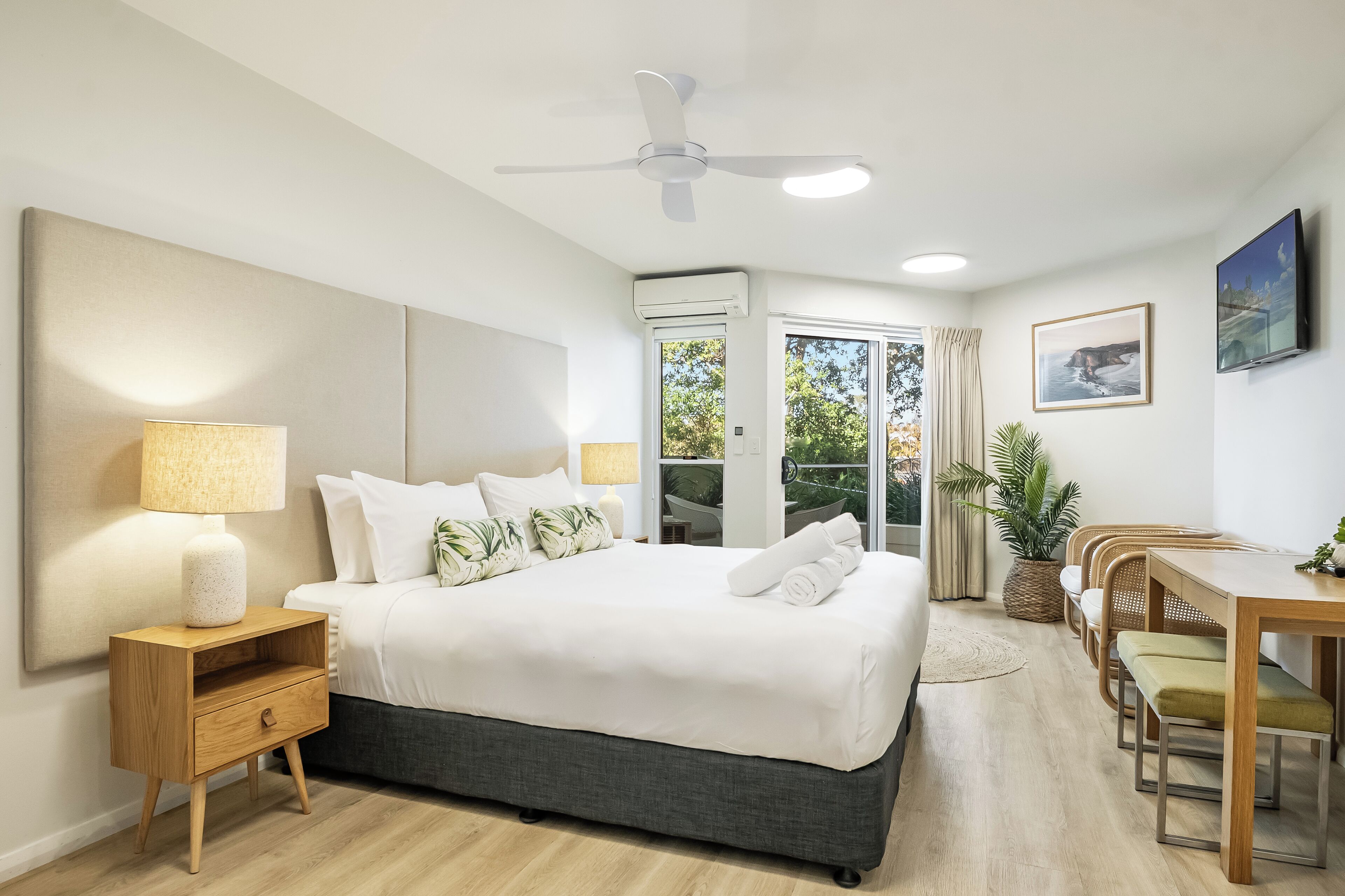 A modern bedroom with a large bed, bedside table, lamp, and a ceiling fan.