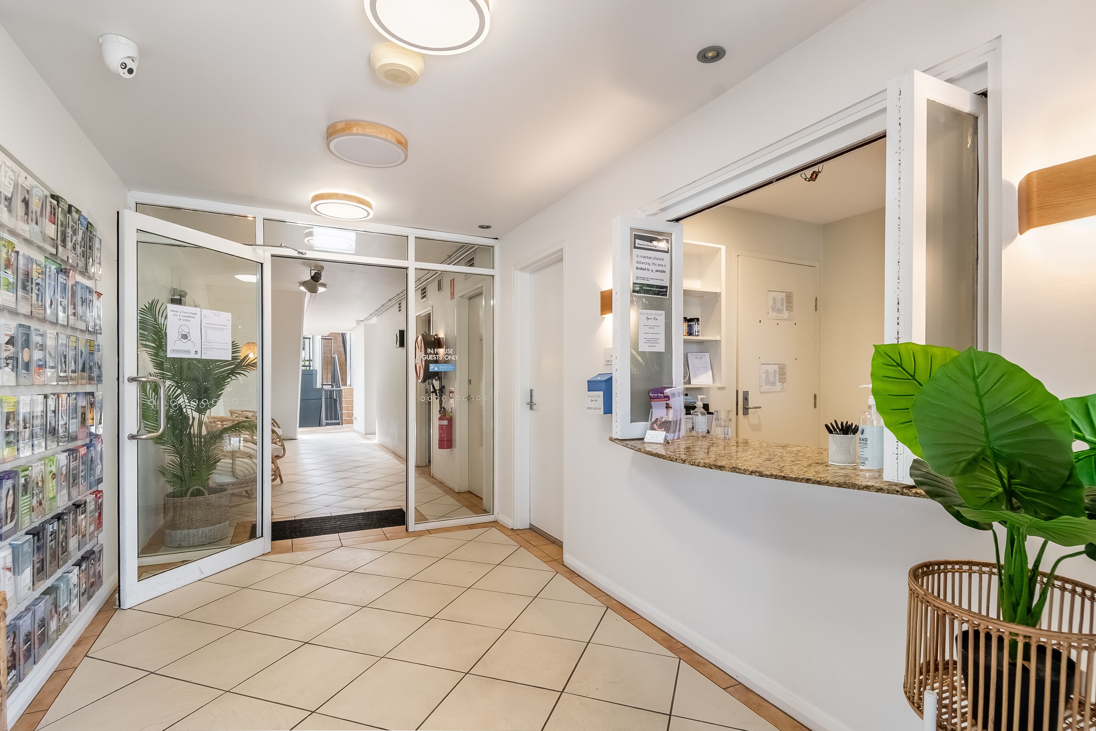 A hotel lobby with a tiled floor, a reception desk, a large mirror, and a wall-mounted security camera.