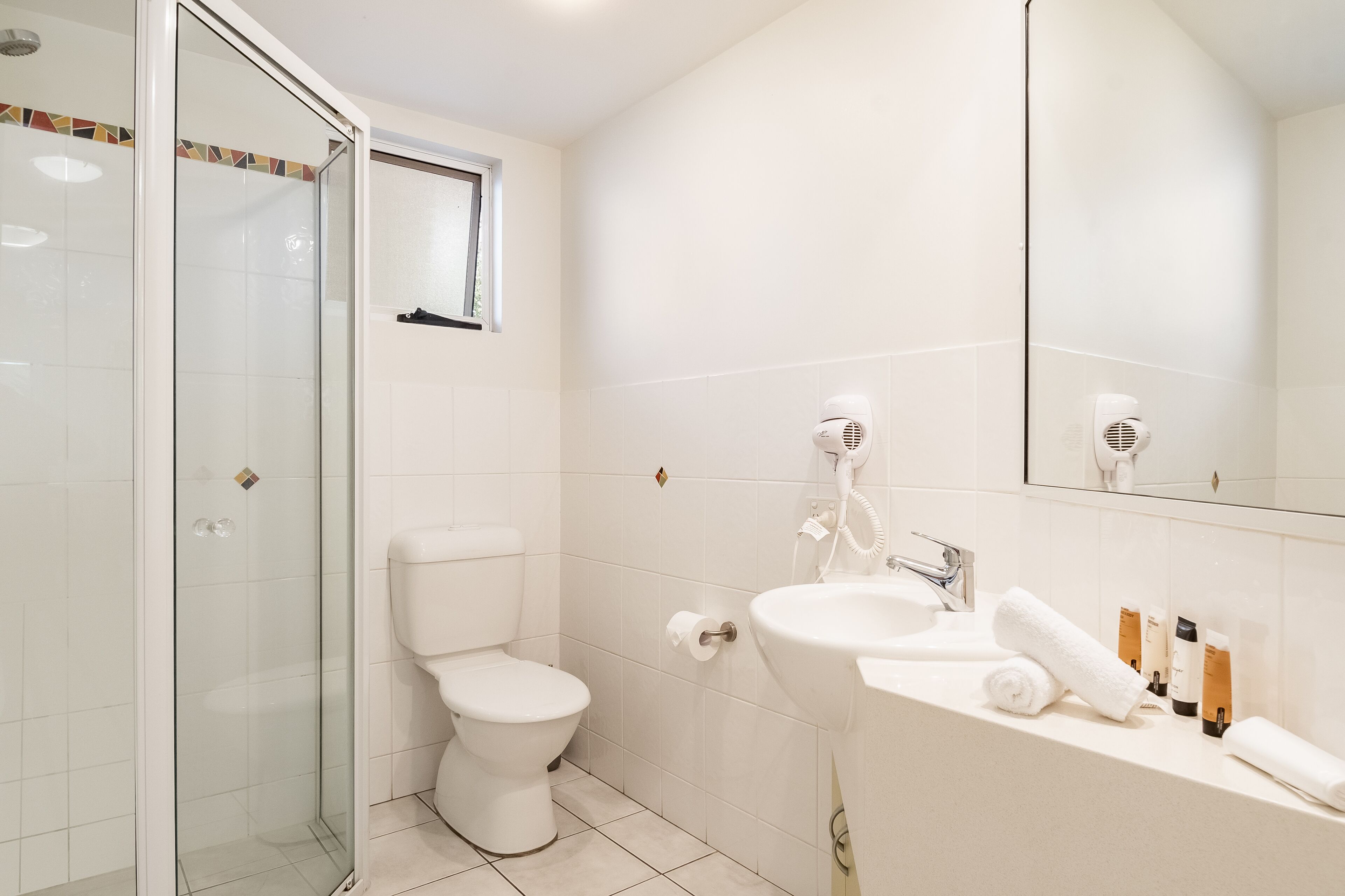 A bathroom with a glass-enclosed shower, a toilet, a sink with a mirror, and toiletries.