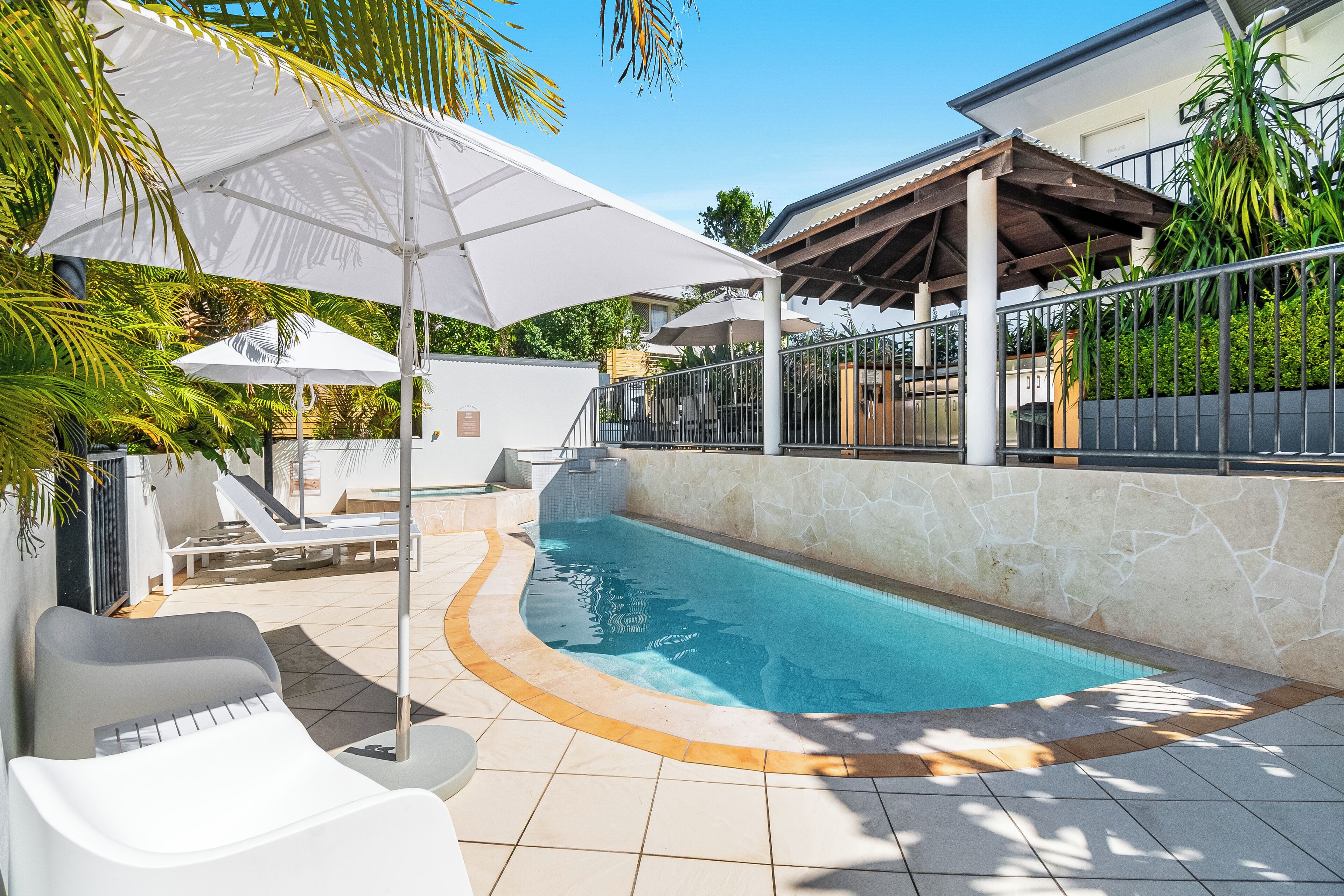A swimming pool with a stone border, white lounge chairs, and umbrellas.