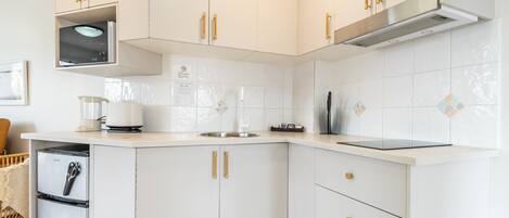 A modern kitchen with white cabinets, gold handles, and a built-in microwave.