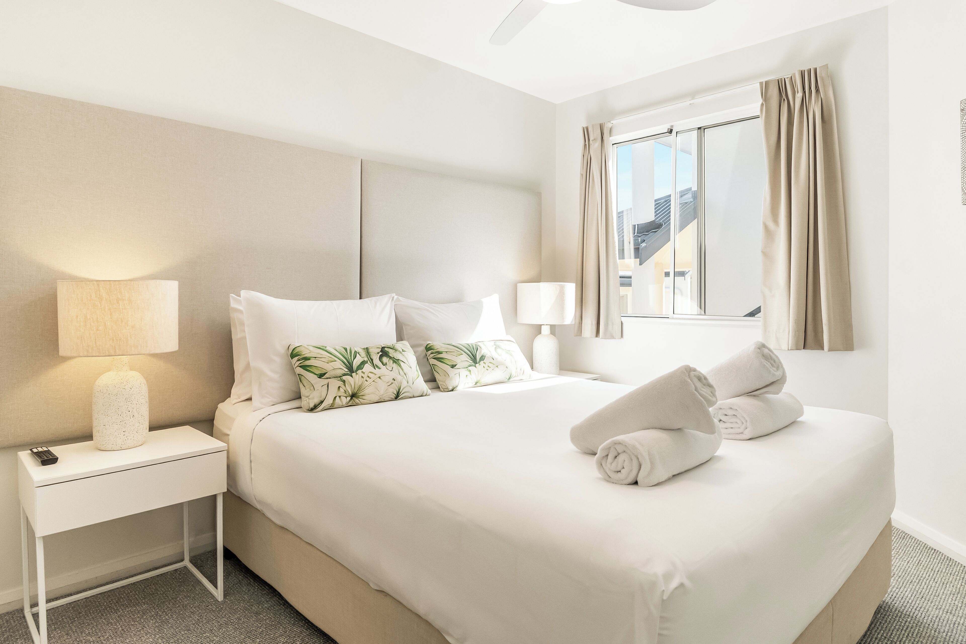 A hotel room with a bed, nightstands, lamps, a window with curtains, and a view of buildings outside.
