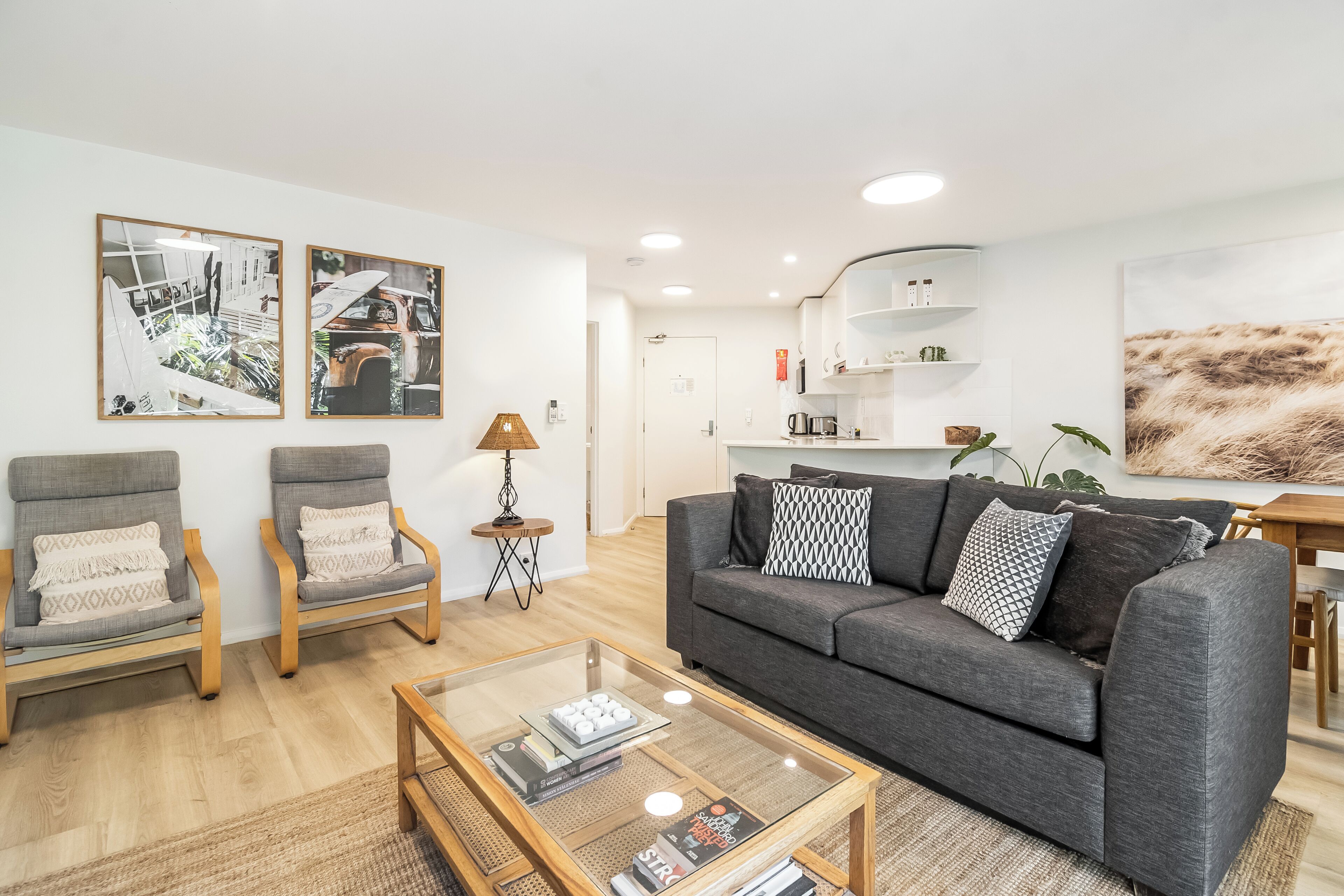 Un salón moderno con un sofá gris, dos sillones, una mesa de centro y una cocina al fondo.