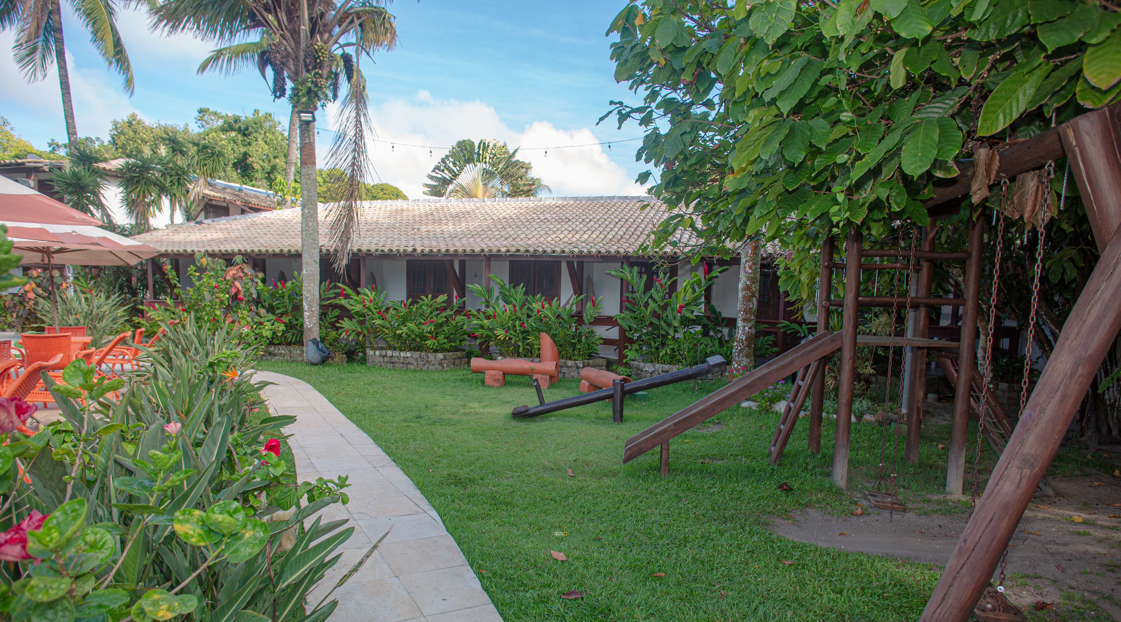 A courtyard with a palm tree, a swing set, and a tiled-roof building.