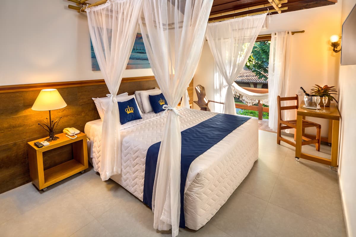 A bedroom with a bed, a bedside table, a lamp, a chair, and a small table with a plant.