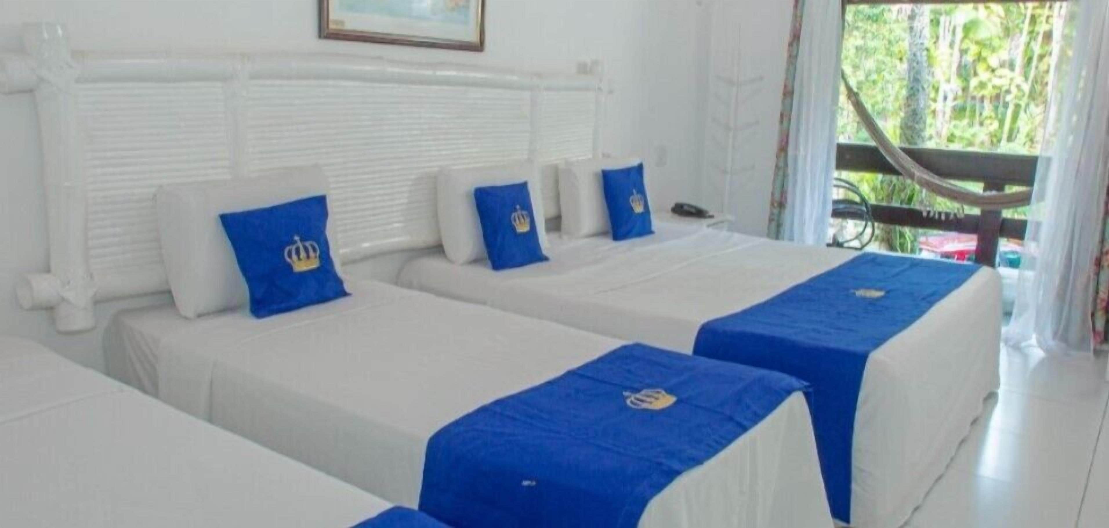 A hotel room with two beds, each with a white headboard and blue bedspreads.