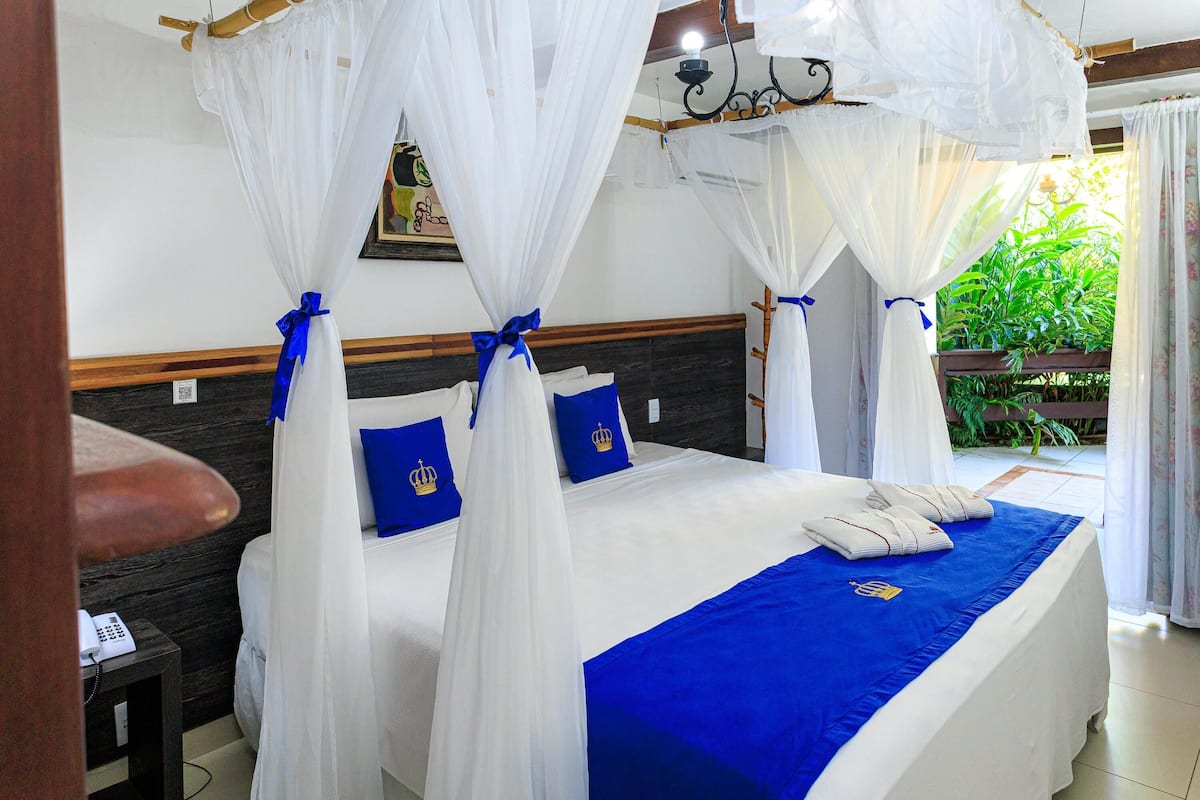 A bed with a canopy, a telephone on a side table, and a view of greenery outside.