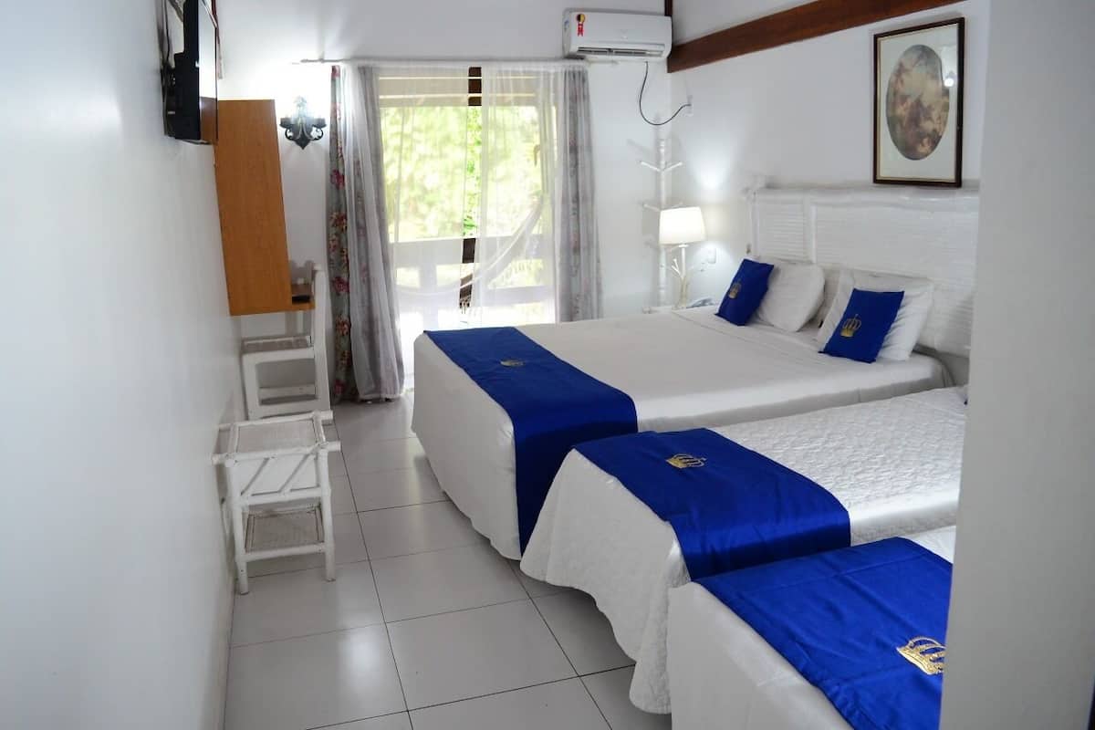 A hotel room with two beds, a small table, a chair, a window with curtains, and a painting on the wall.