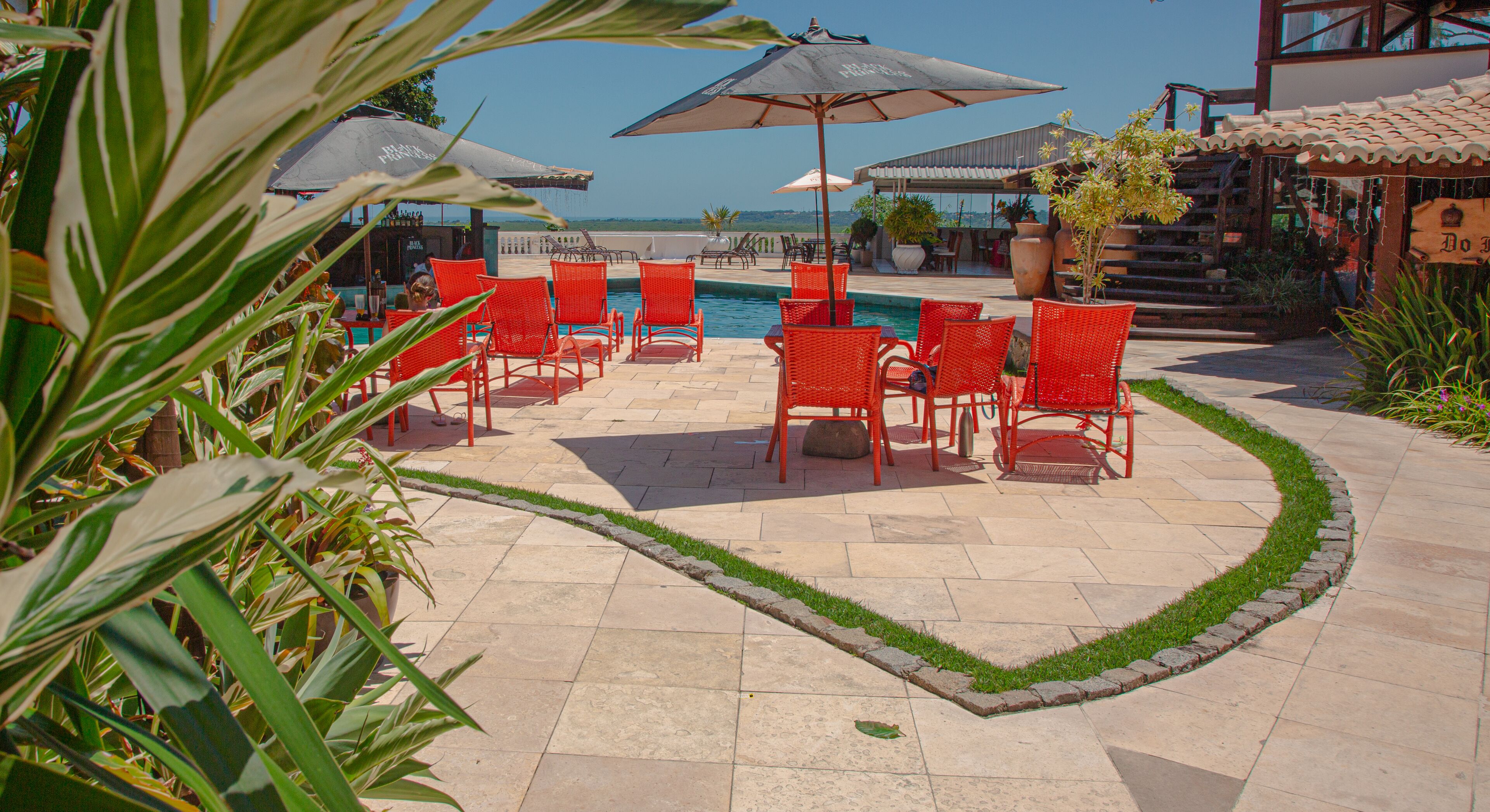 A poolside area with red chairs and umbrellas, a pool, and a view of the ocean.