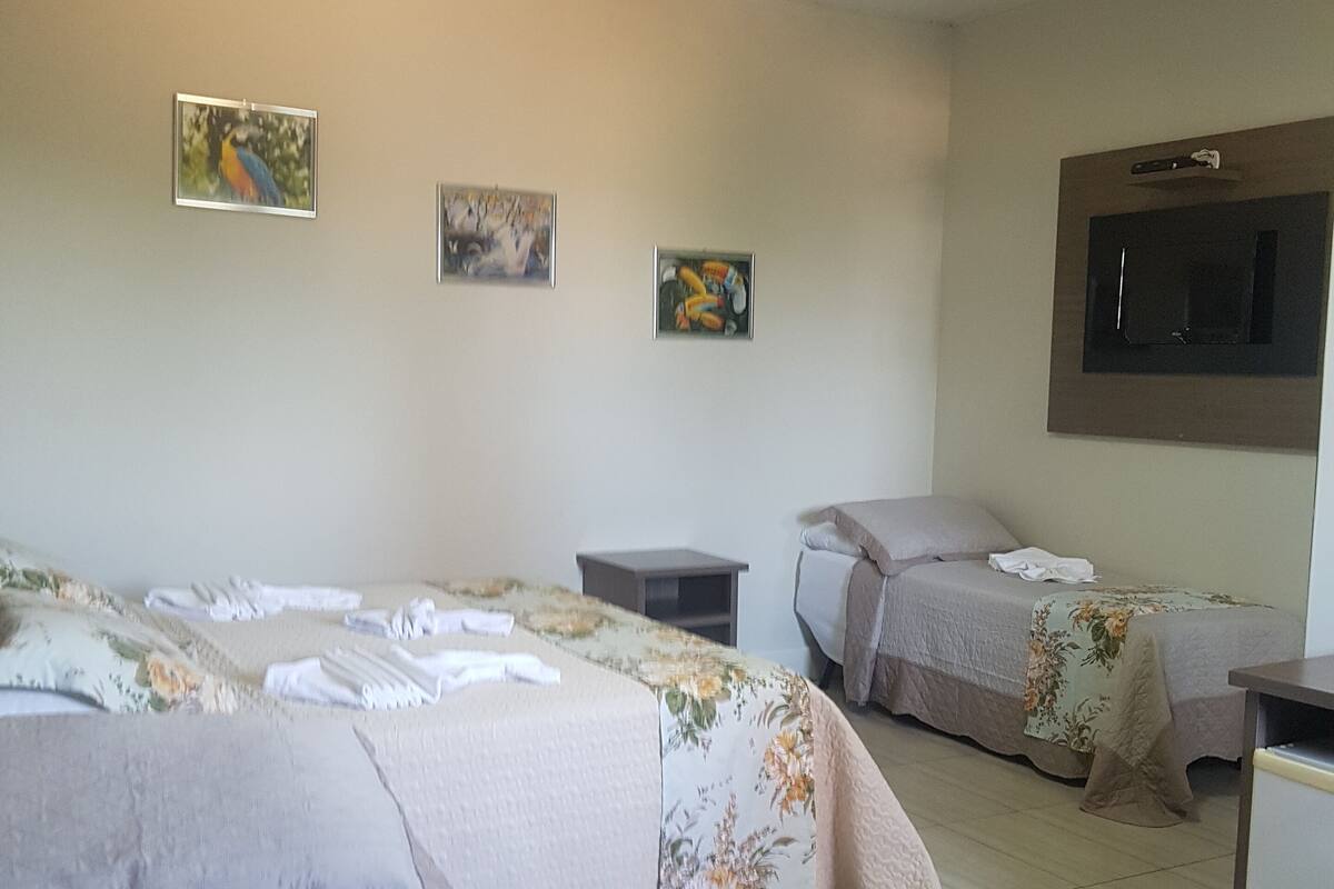 A hotel room with two beds, a small table, and a TV mounted on the wall.