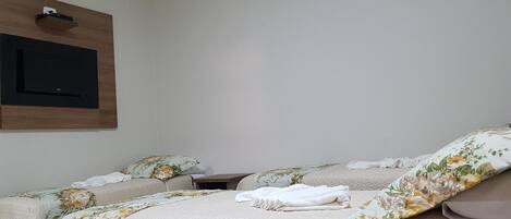 A hotel room with two beds, a flat-screen TV mounted on the wall, and a wooden panel above the TV.
