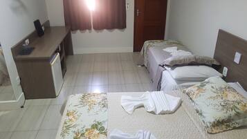 Quarto de hotel com duas camas, uma escrivaninha, um guarda-roupa e uma janela com cortinas.