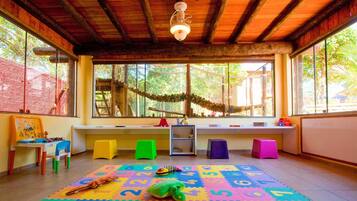 Una habitación con techo de madera, ventanas amplias, un tapete de juego colorido con números y un taburete pequeño verde.