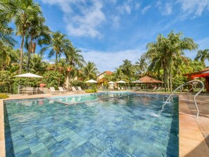 Uma piscina com água cristalina, rodeada por palmeiras e espreguiçadeiras.