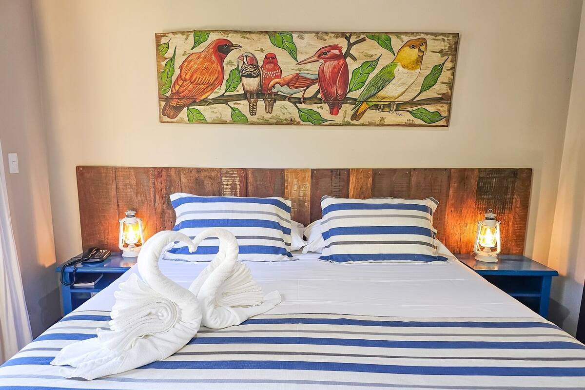 A hotel room with a bed featuring striped bedding, two bedside tables with lanterns, and a wall-mounted painting of birds.