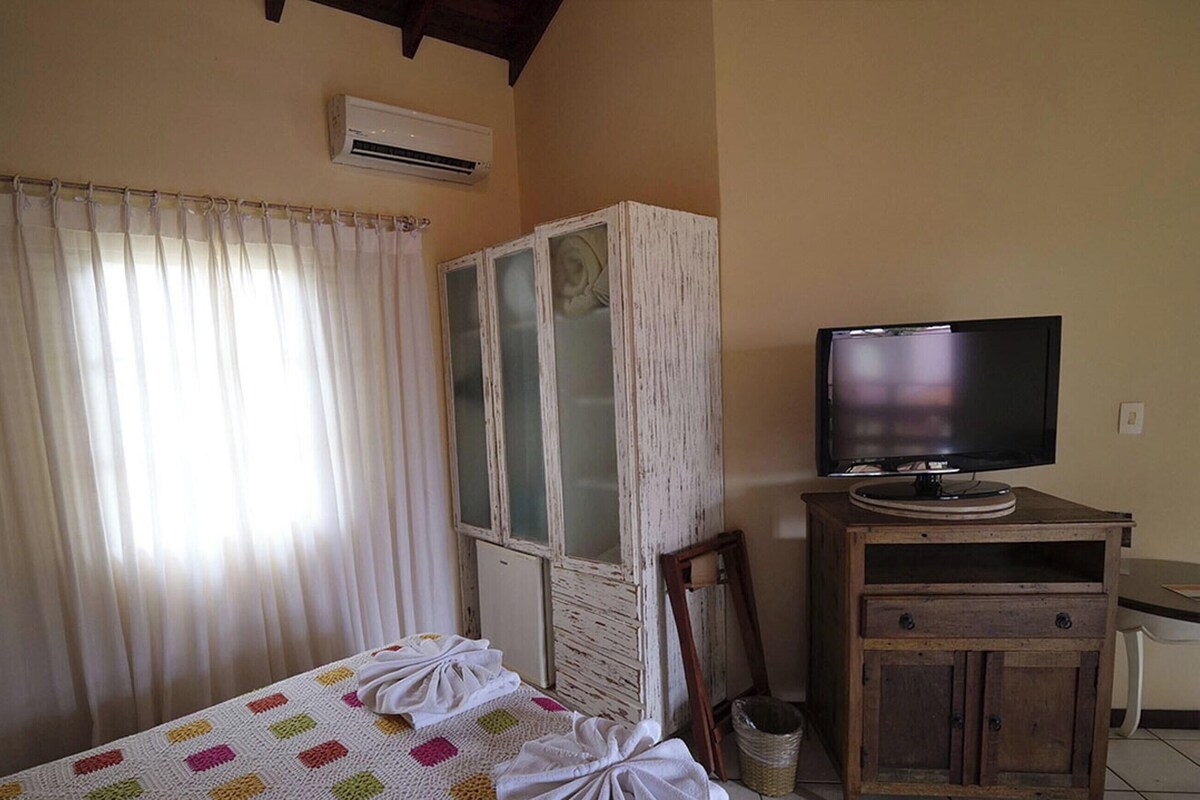 A room with a bed, a television on a wooden stand, a cabinet, and a window with curtains.