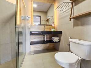 Um banheiro moderno com box de vidro, pia com bancada preta, vaso sanitário e toucador de madeira.